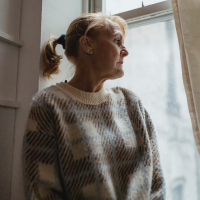 frustrated older woman in sweater by window